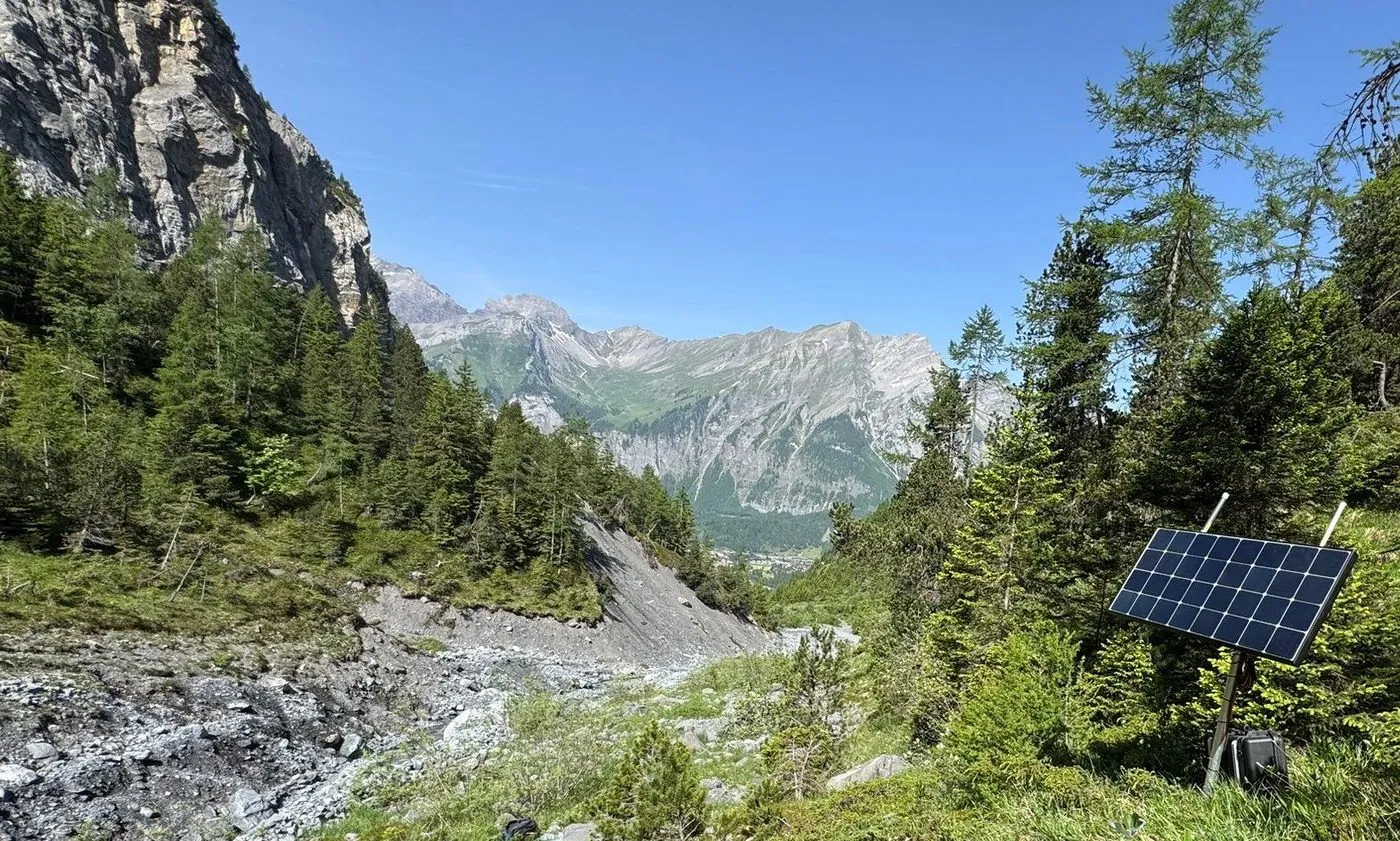 A debris flow channel cutting through an Alpine valley, with a Seismicstream station on the slope above it