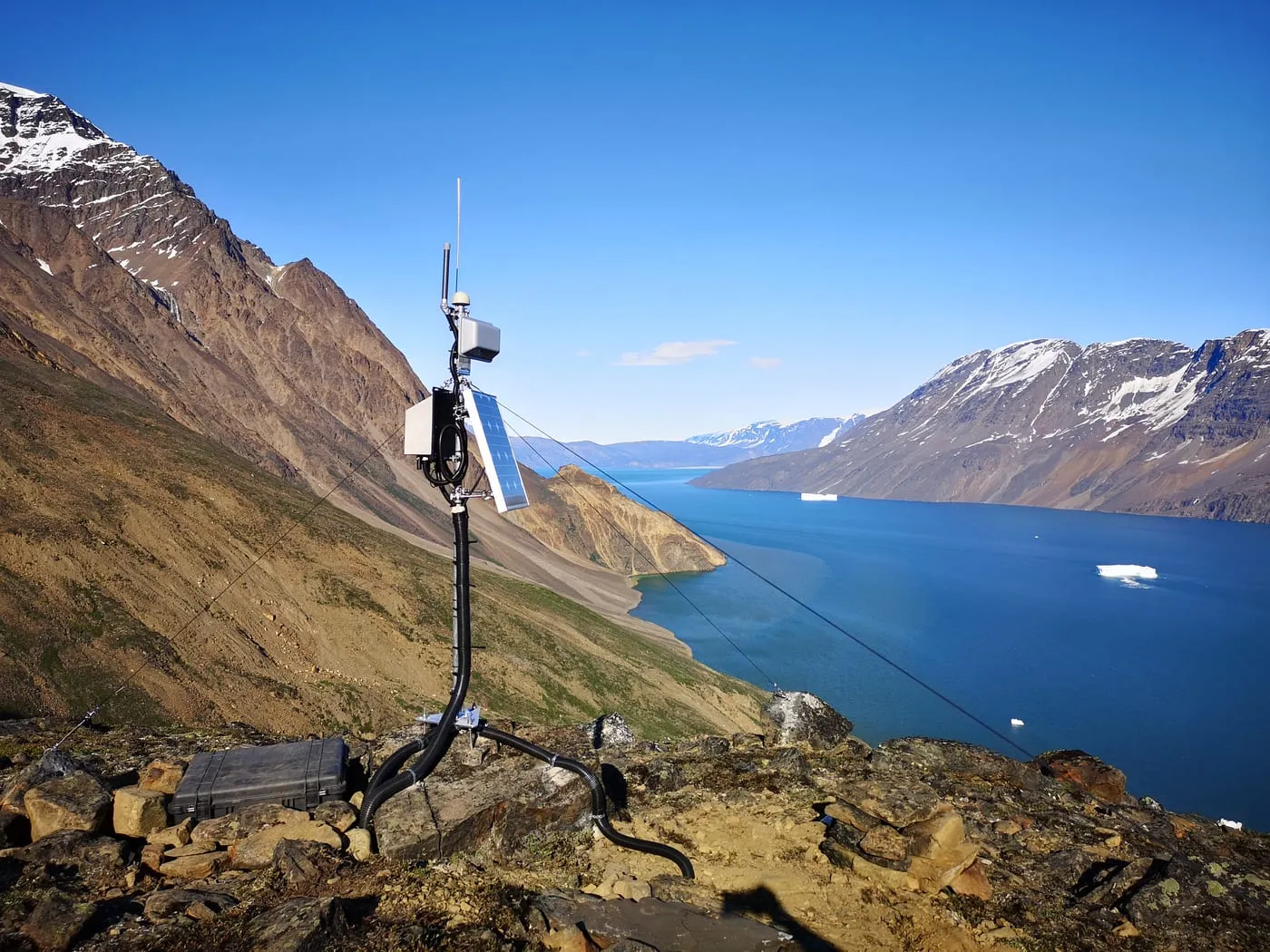 A solar-powered Seismicstream mast with radio and GNSS antennas above a fjord